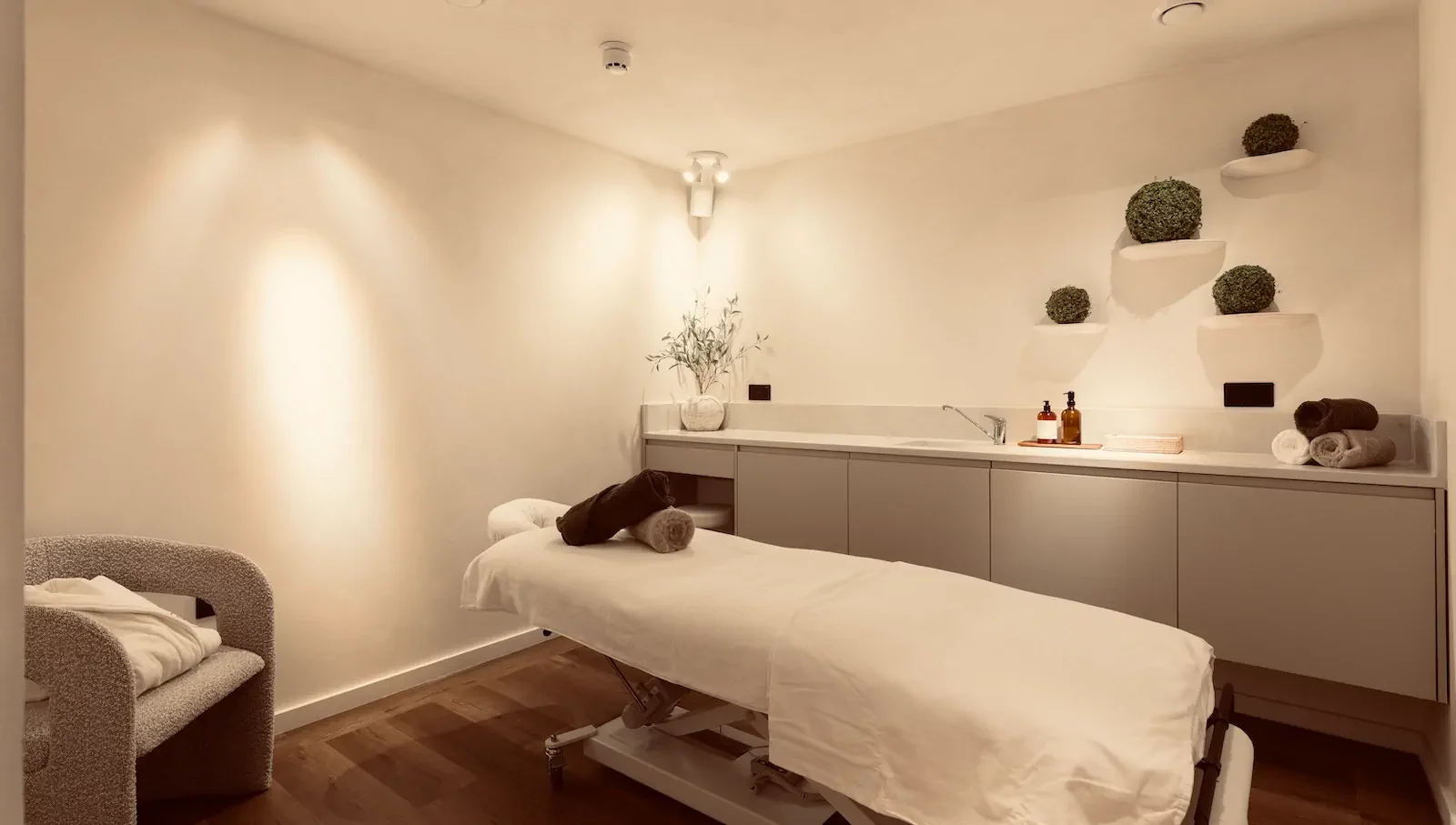 Tranquil massage treatment room with white table, ambient lighting, and wellness products.