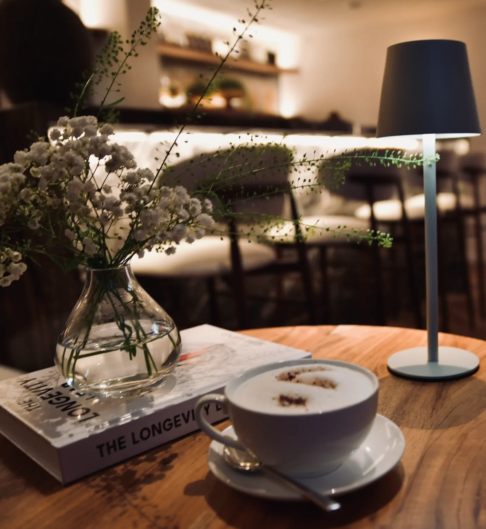 Comfortable lounge area with longevity book, coffee, and fresh flowers on wooden table.