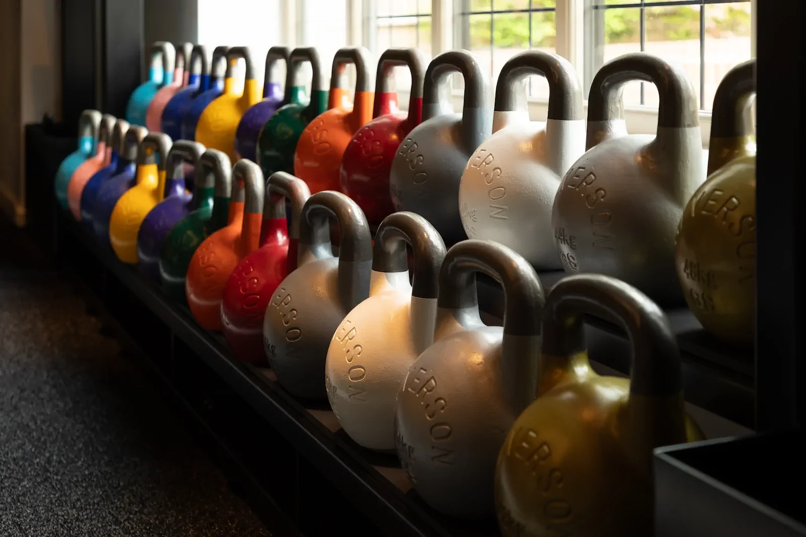 Collection of colorful kettlebells arranged by weight on fitness equipment rack.