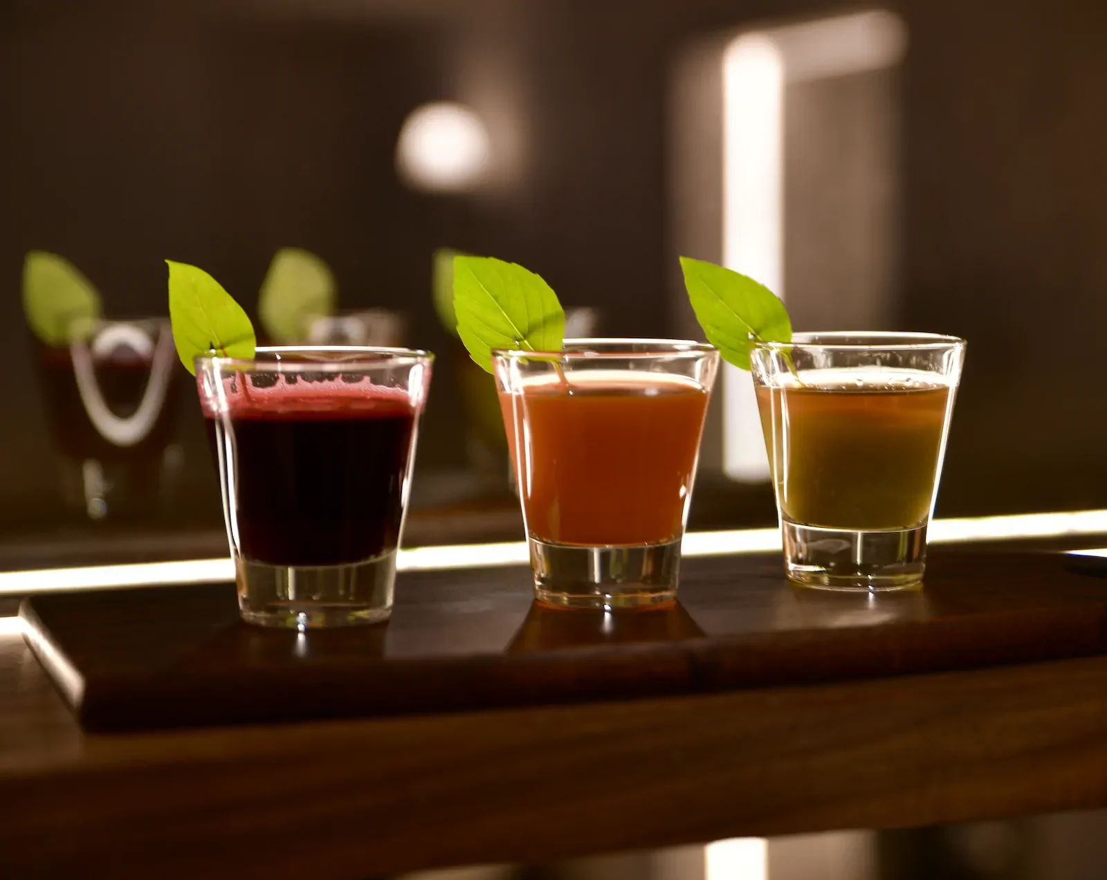 Three wellness juice shots in different colors garnished with fresh green leaves.