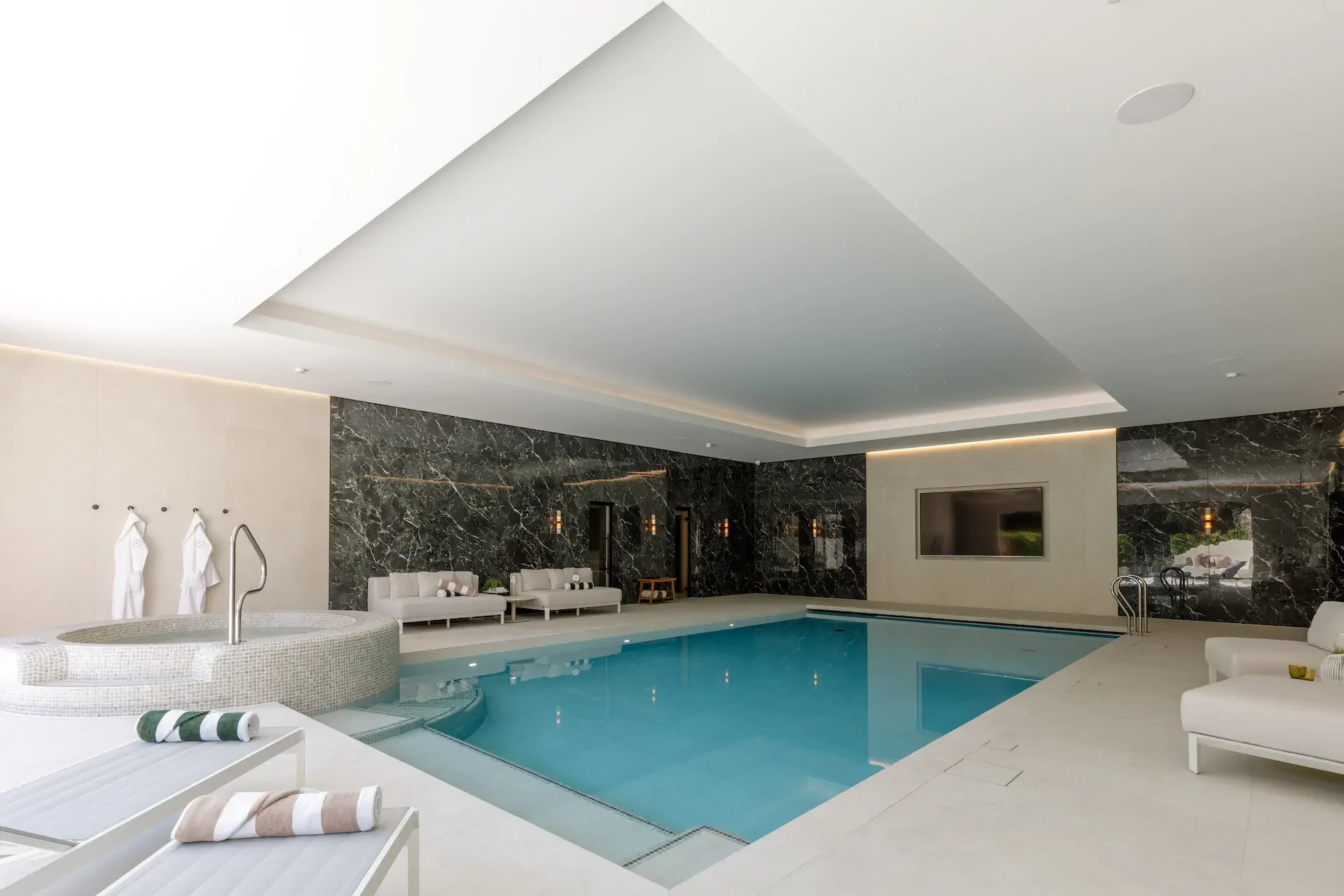 Luxurious indoor pool with marble walls, white loungers, and spa-like atmosphere.