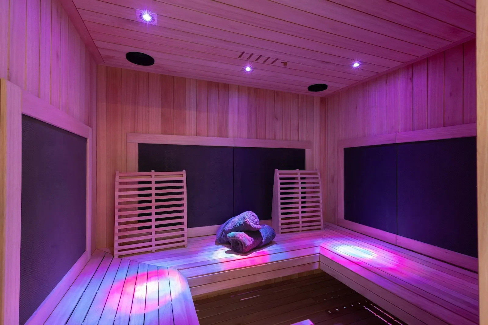Modern sauna with wood paneling, purple ambient lighting, and tiered seating.