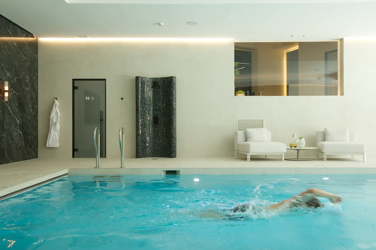 Indoor swimming pool with person exercising, marble walls, and spa relaxation area.
